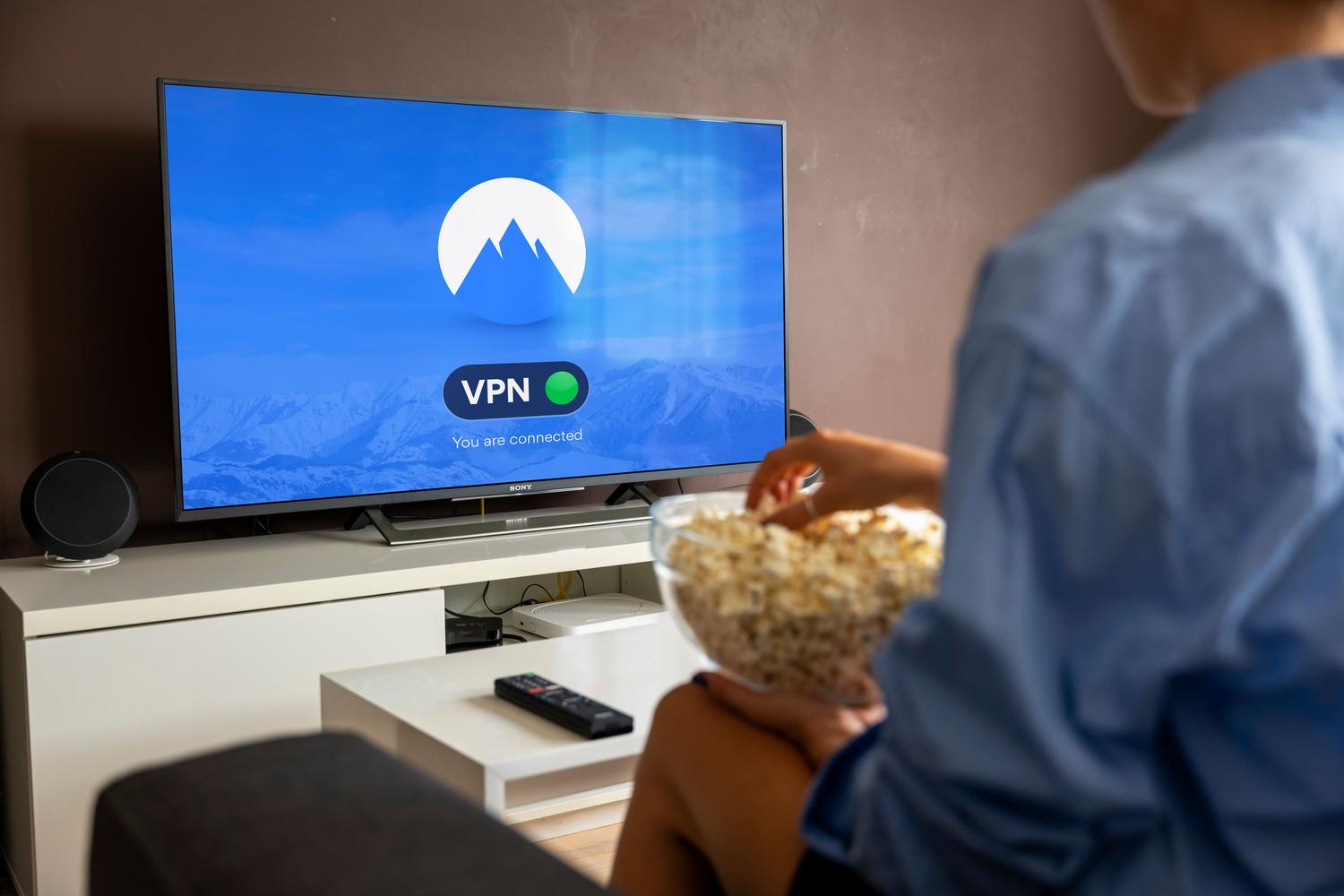 Persona relajada en casa comiendo palomitas mientras ve la televisión con una VPN activada para acceder a contenidos de streaming.
