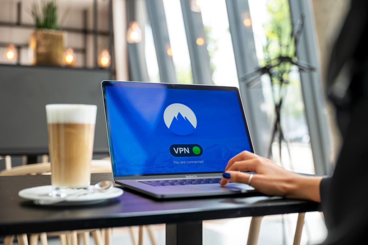 Persona utilizando una VPN en su portátil en una cafetería para navegar de forma segura en redes públicas y evitar restricciones.